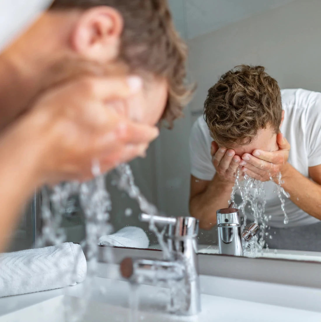 A man washes his face at a bathroom sink.