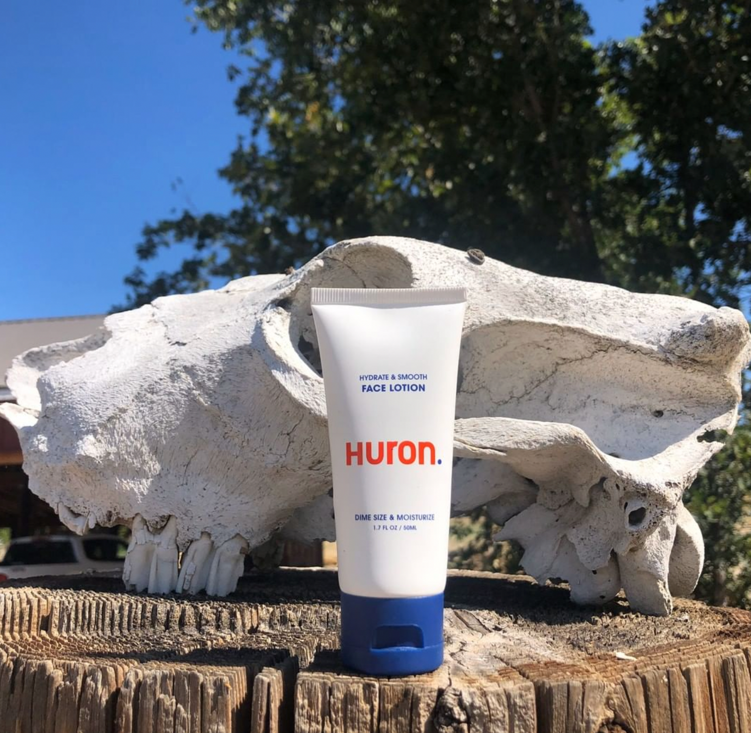 A tube of face lotion sits on a wooden stump outdoors.