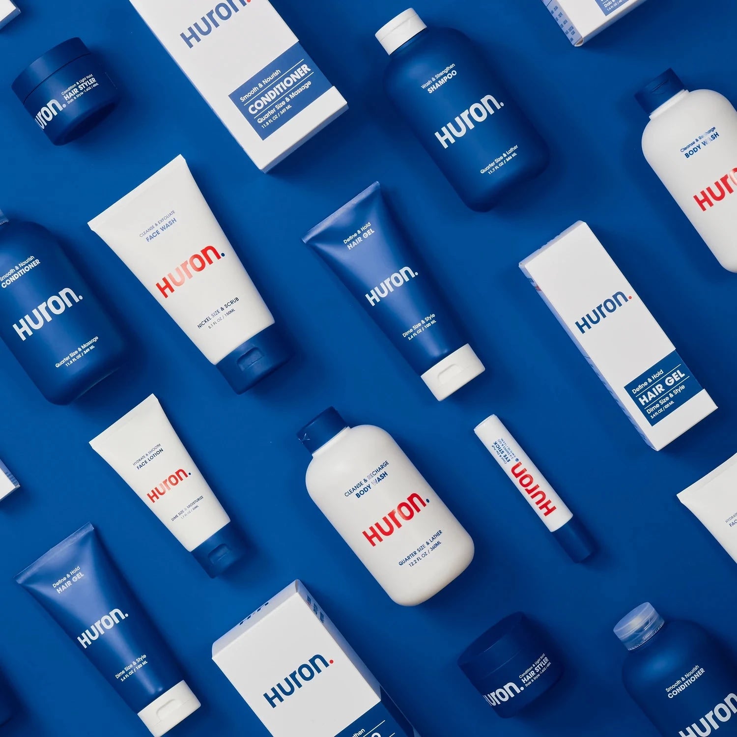 An assortment of hair, body, and face care tubes and boxes lie flat against a blue background. 