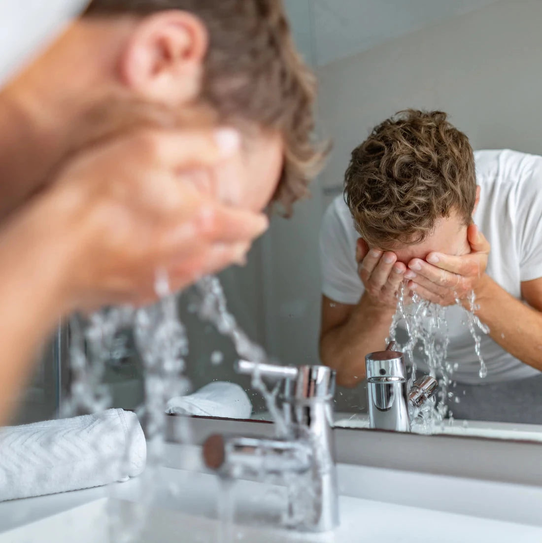 A man washes his face at a bathroom sink. 