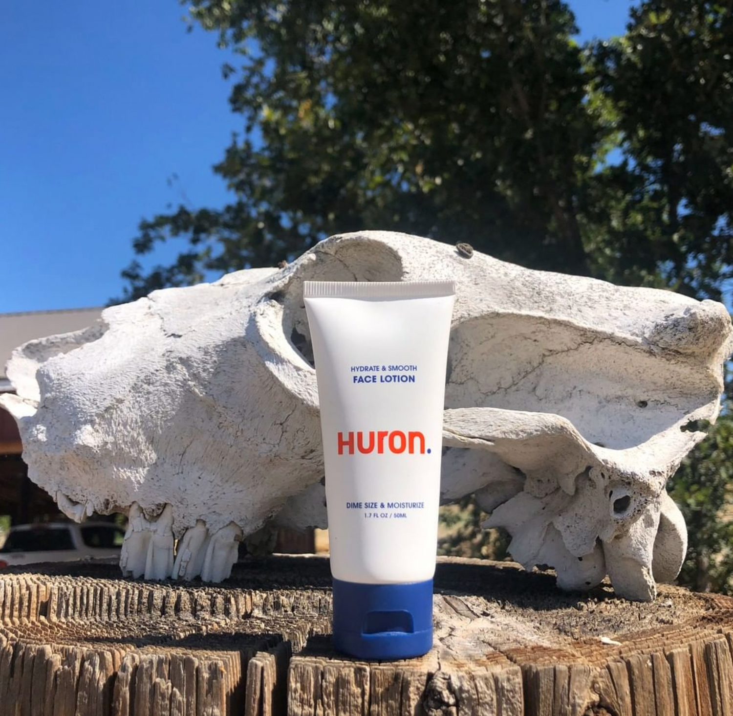 A tube of face lotion sits on a wooden stump outdoors. 