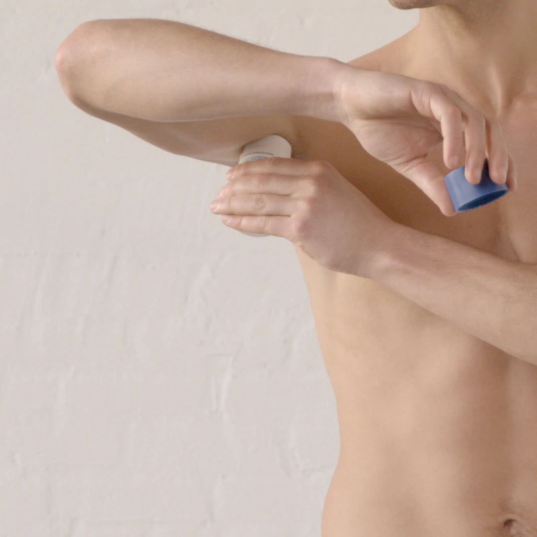 A man applies deodorant to his underarm. 