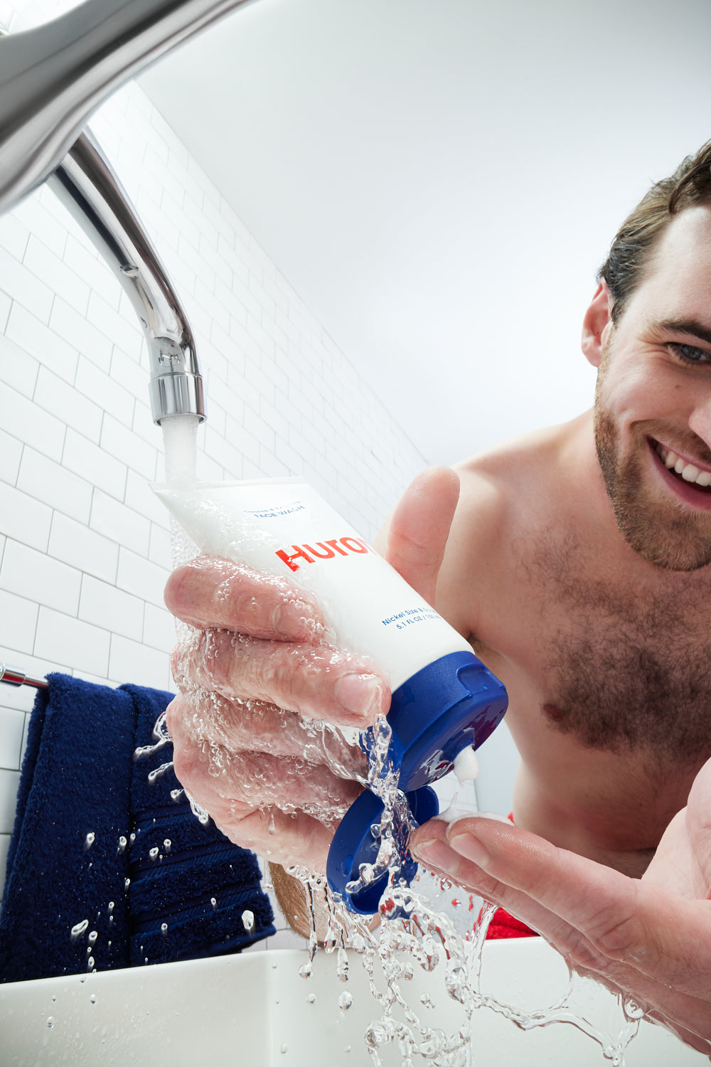 A man uses a face wash in a bathroom sink. 