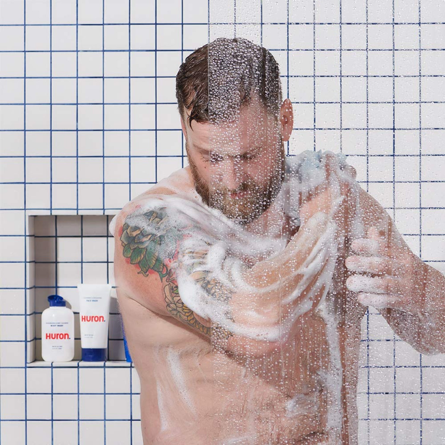 A man lathers up using body wash in the shower. 