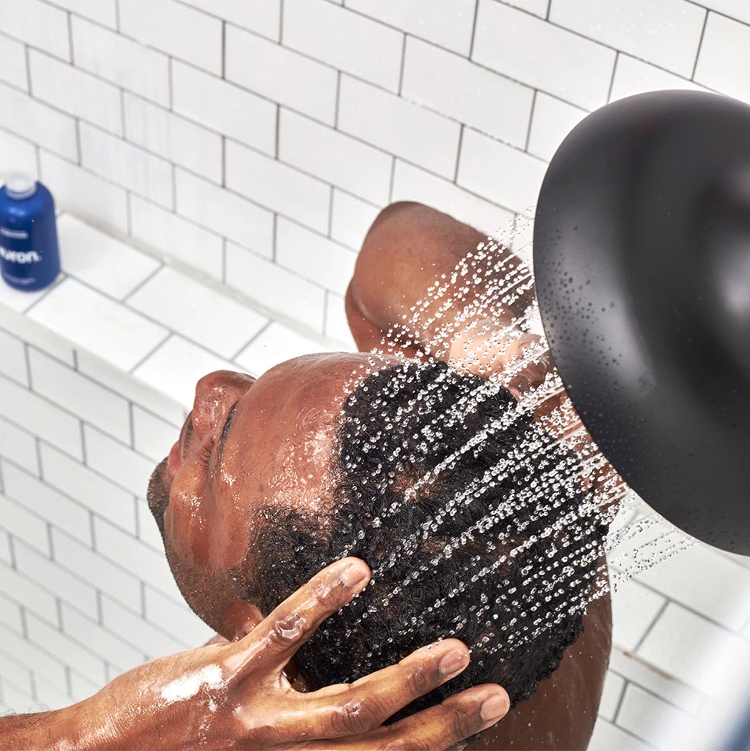 A top-down view of a man washing his hair in a white tiled shower. 